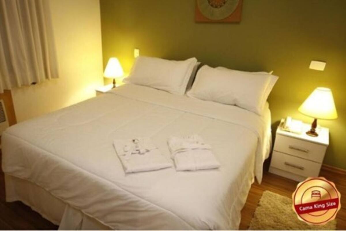 A neatly made bed with white linens and pillows, a bedside table with a lamp, and a small rug on the floor.