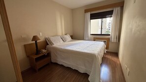 A bedroom with a bed, bedside table, lamp, and a window with curtains. - London Class Hotels (São Paulo)