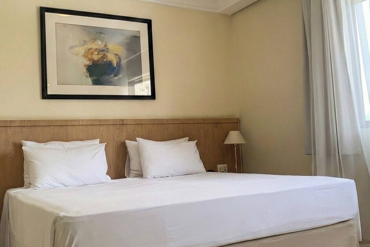 Een hotelkamer met een groot bed, een hoofdbord, een ingelijst beeld aan de muur, een bedlampje en een raam met gordijnen.