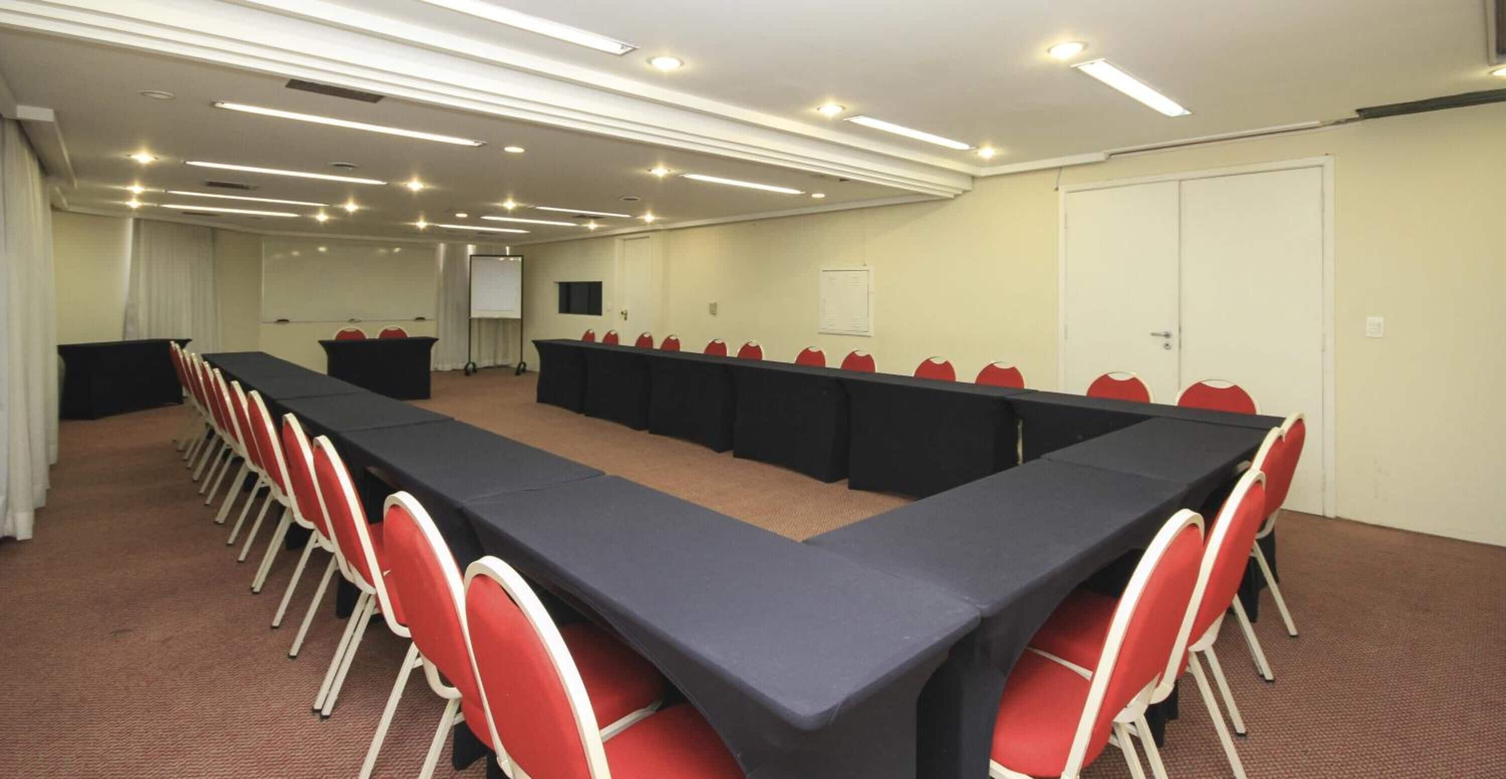 A conference room with a long table, red chairs, and a projector screen.