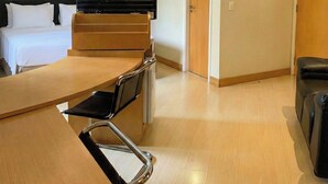 Une chambre d’hôtel avec un lit, un bureau et une chaise, une télévision et une porte.
