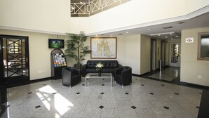 Un hall d’entrée avec un canapé en cuir noir, une table basse, un téléviseur, une plante et une carte encadrée accrochée au mur.