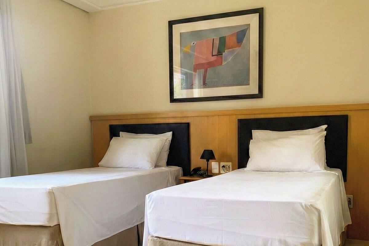 Hotelkamer met twee bedden, een houten hoofdbord, een lijst met een abstract schilderij en een nachtkastje met een lamp.