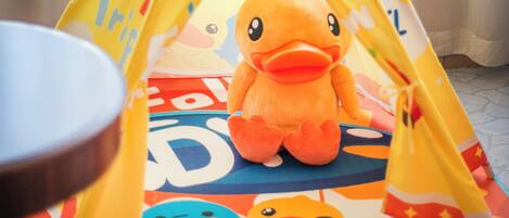 A colorful play tent with a duck design, a plush toy duck, and a pair of baby shoes.