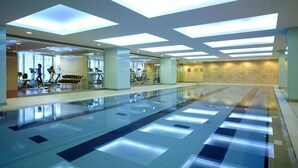 A spacious indoor swimming pool with a glass wall on one side, allowing views of the gym area with exercise equipment. - Shangri-La Changchun (Changchun)