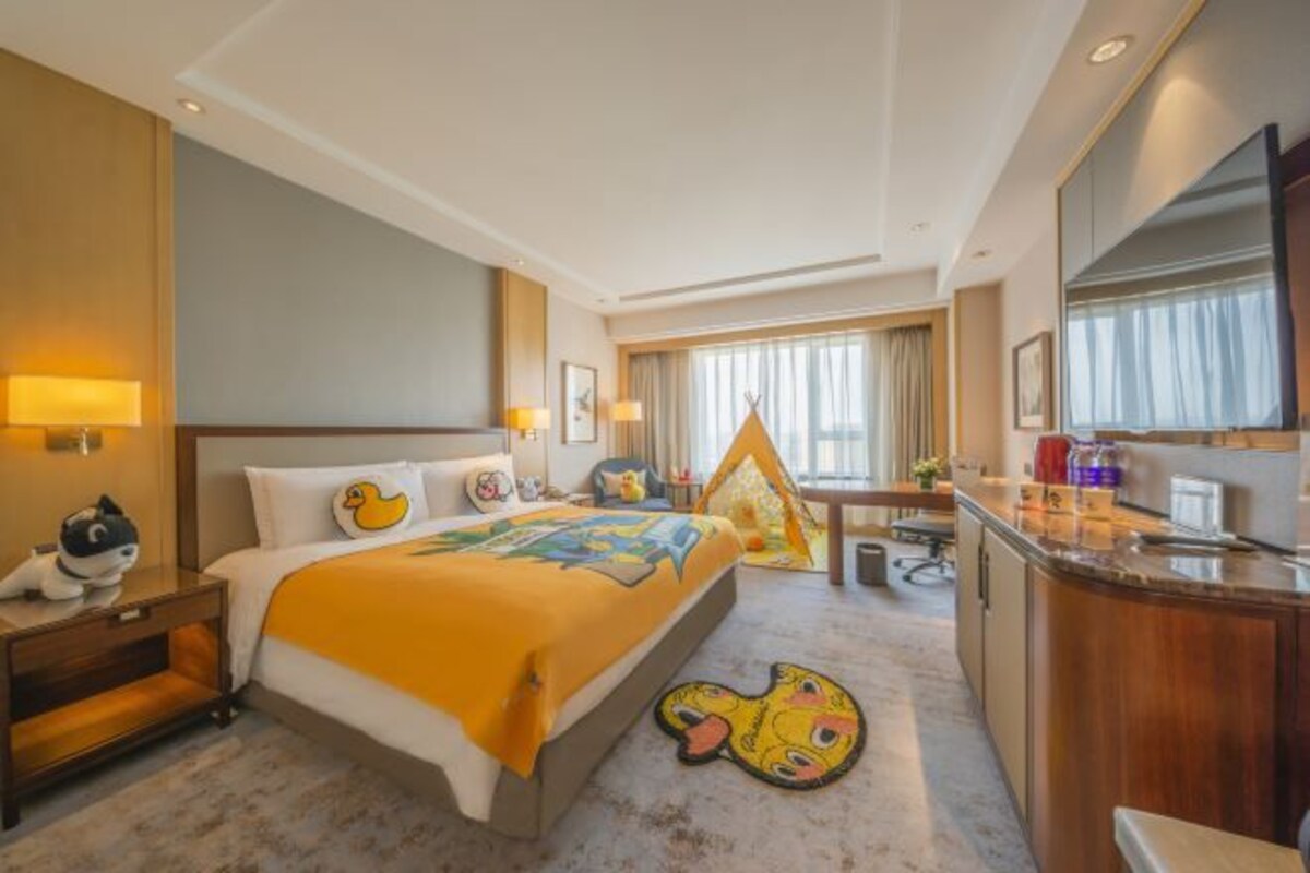 A hotel room with a bed, a desk, a chair, a TV, and a window.
