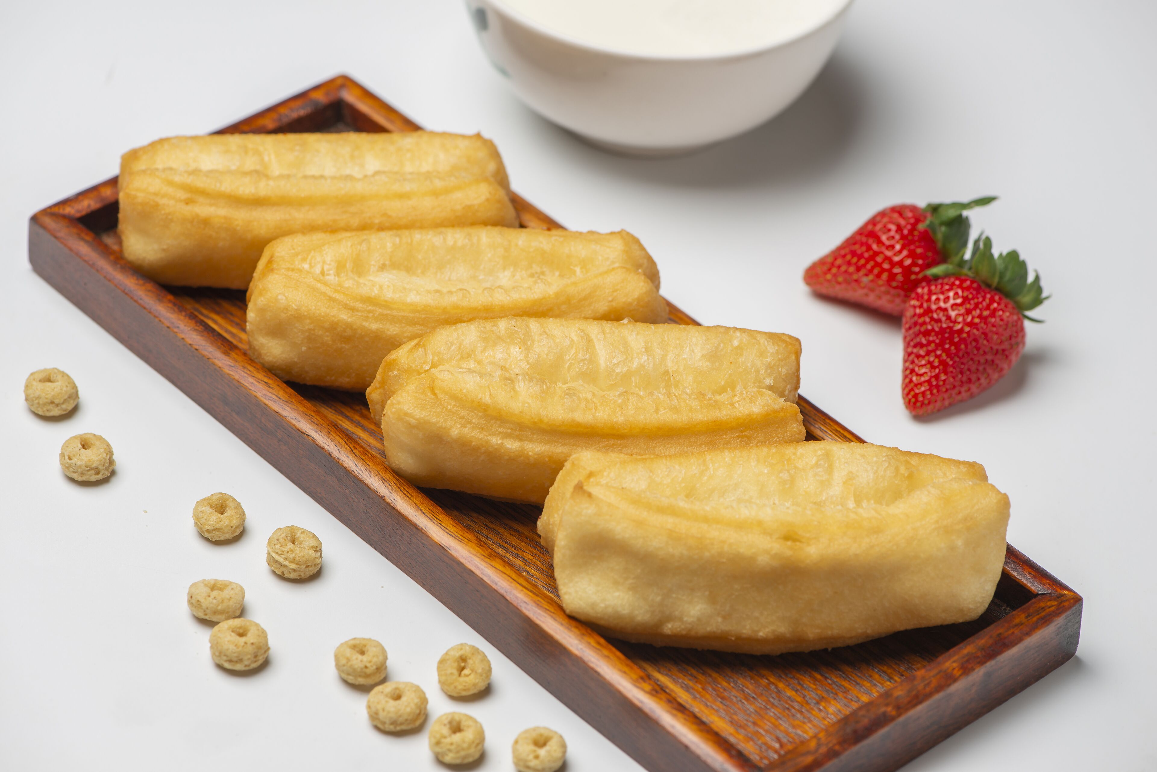 Un vassoio di legno con diversi dolci e qualche fragola su una superficie bianca.