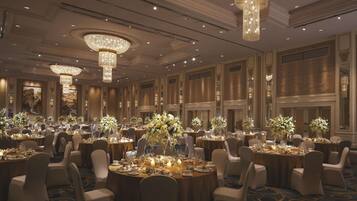 A banquet hall with round tables, chandeliers, and floral centerpieces.