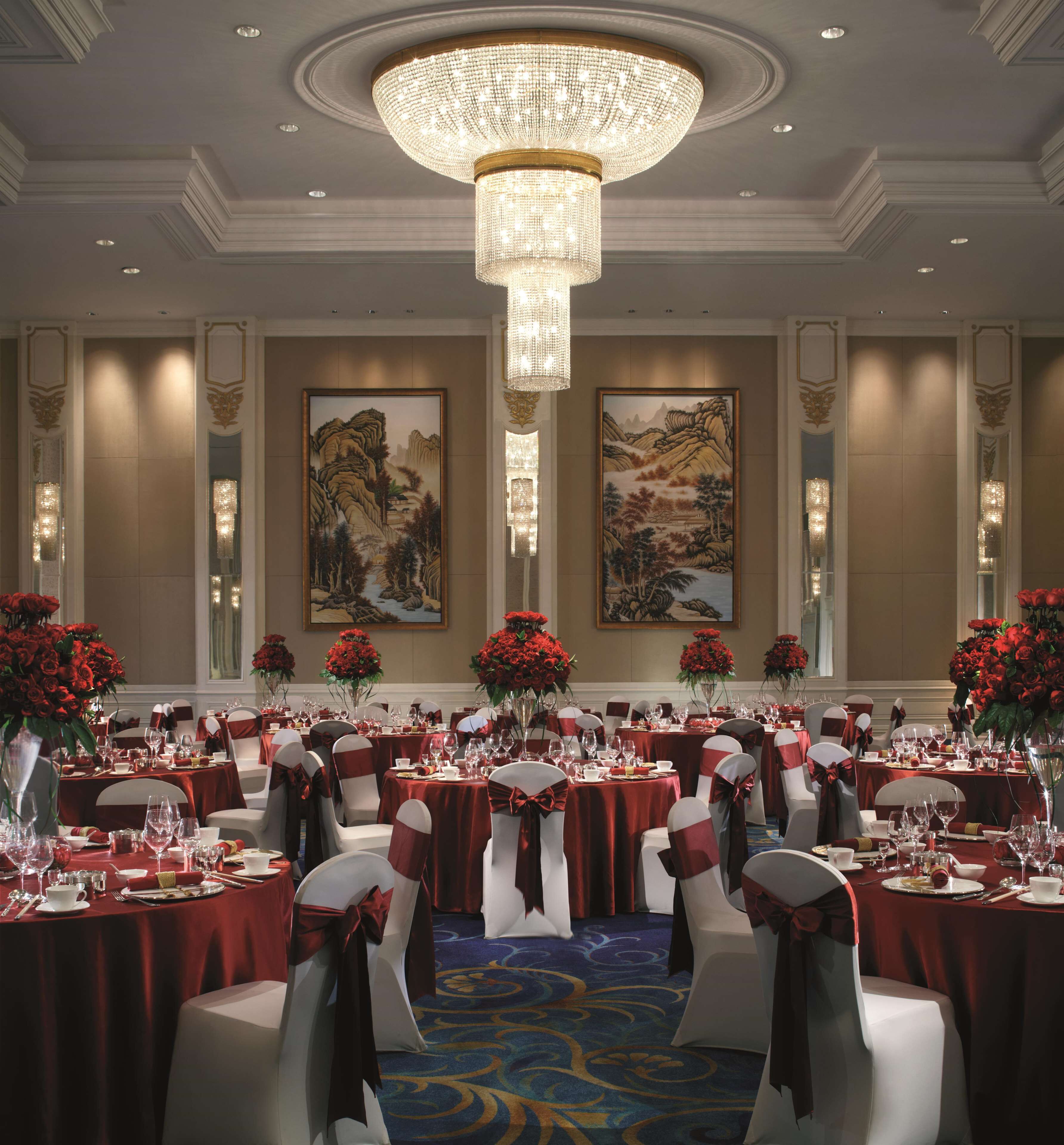 Une salle de banquet avec des tables rondes, des nappes rouges et des chaises blanches ornées de rubans rouges.