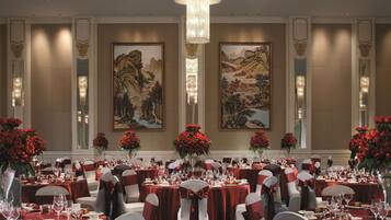 Une salle de banquet avec des tables rondes, des nappes rouges et des chaises blanches ornées de rubans rouges.
