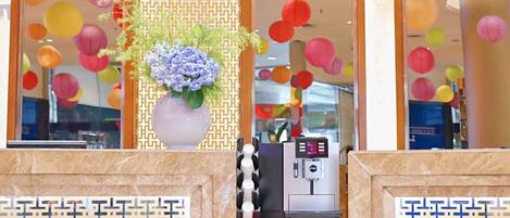 A reception area with a coffee machine, a decorative vase with flowers, and colorful paper lanterns in the background.