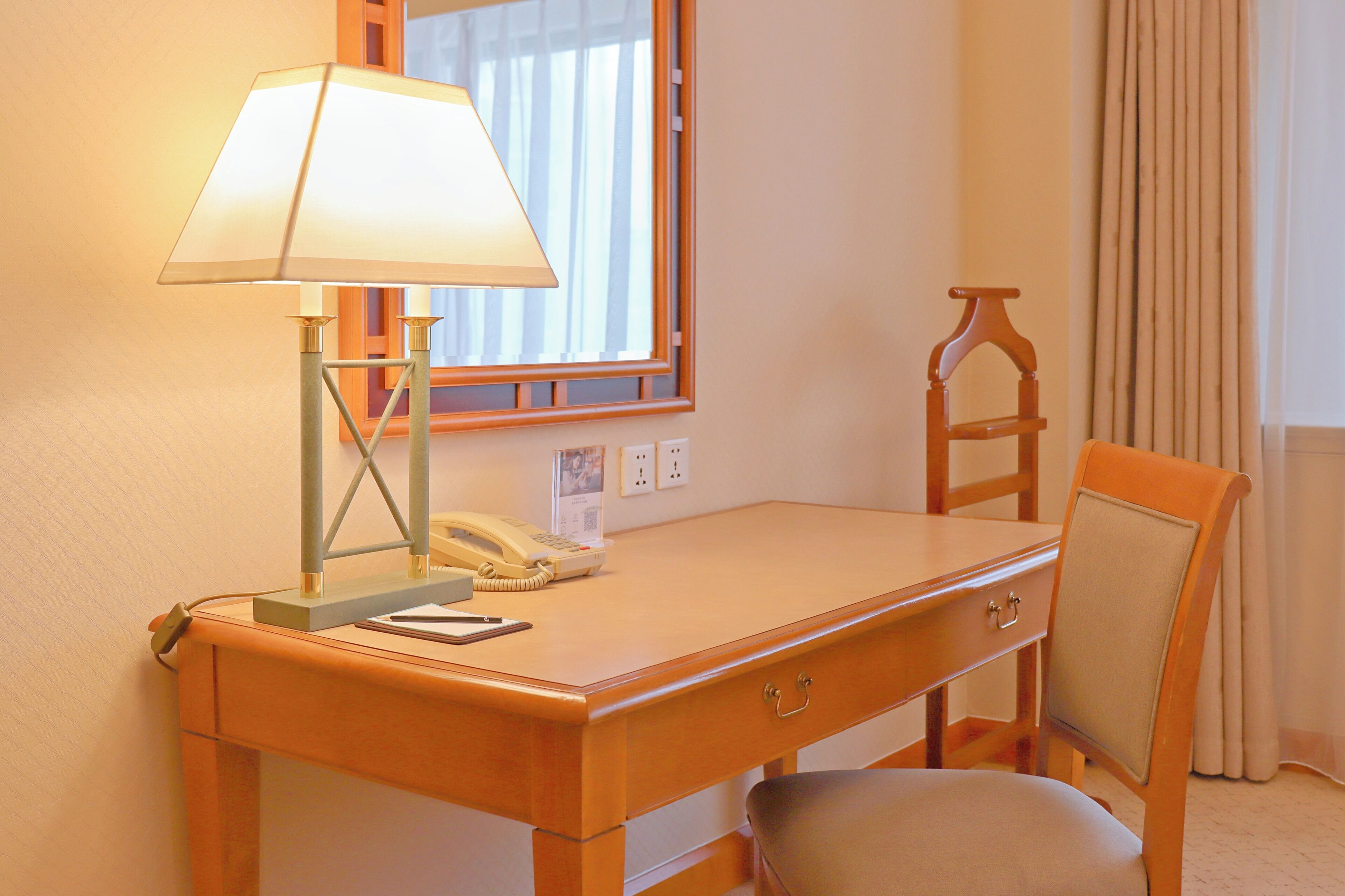 Una habitación de hotel con un escritorio de madera, una lámpara, un teléfono y una silla.