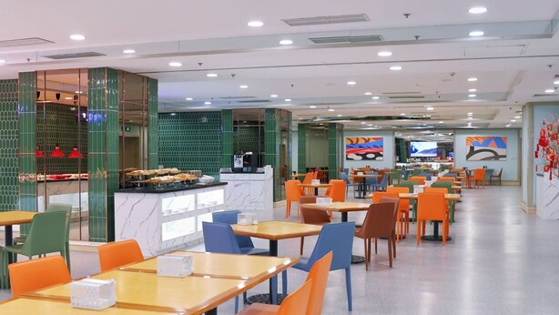 A spacious cafeteria with multiple tables and chairs, a counter with food items, and a television screen in the background. - JEN Shenyang by Shangri-La (Shenyang)