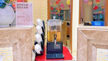 Estación autoservicio de bebidas con una máquina de café, dispensador de agua y un cartel que indica bebidas calientes disponibles.