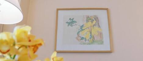 A framed artwork on a wall, a lamp, and yellow flowers in the foreground.