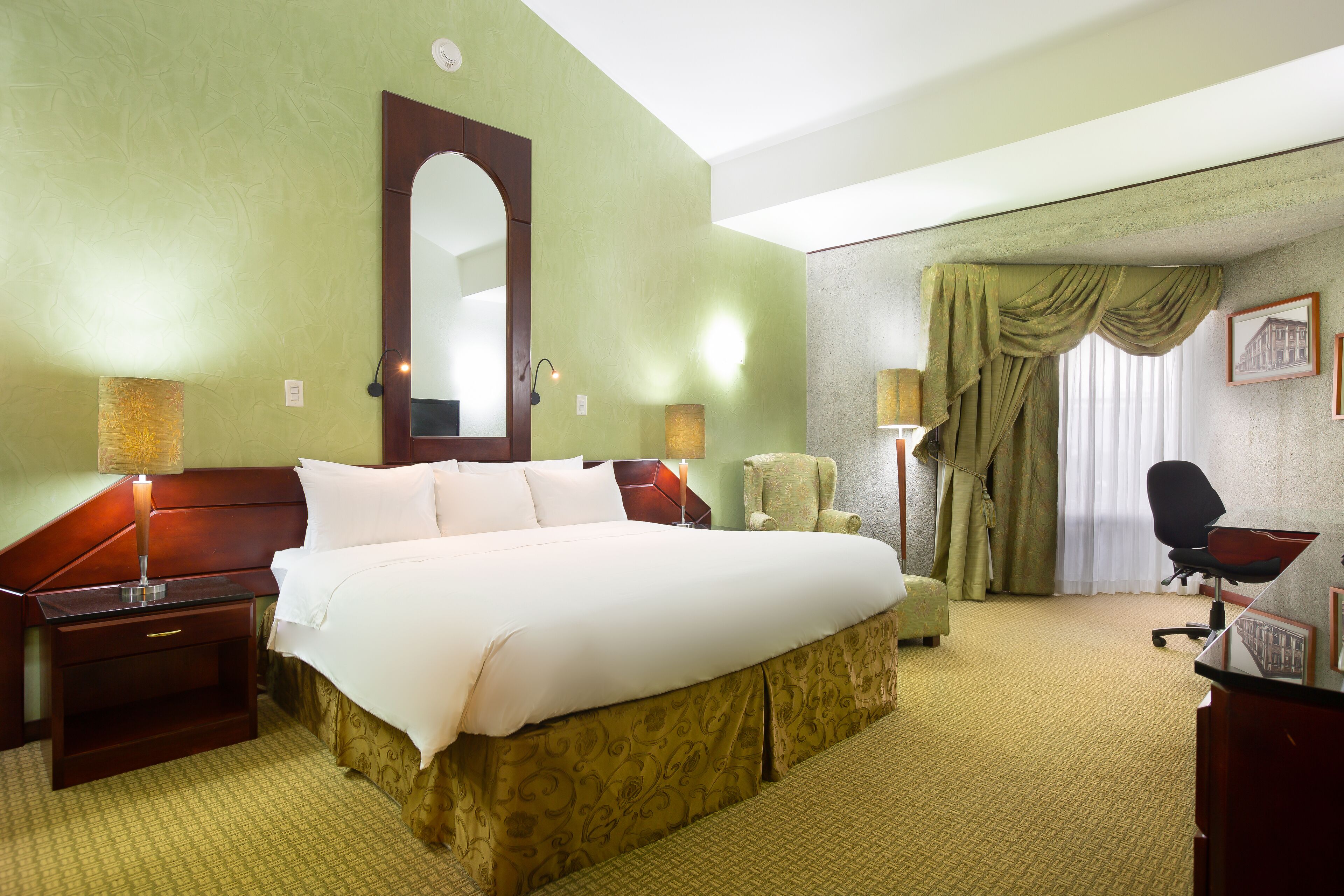 A hotel room with a large bed, a desk, a chair, a lamp, and a picture on the wall.