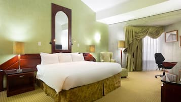 Habitación de hotel con una cama grande, un escritorio, una silla, una lámpara y un cuadro en la pared.