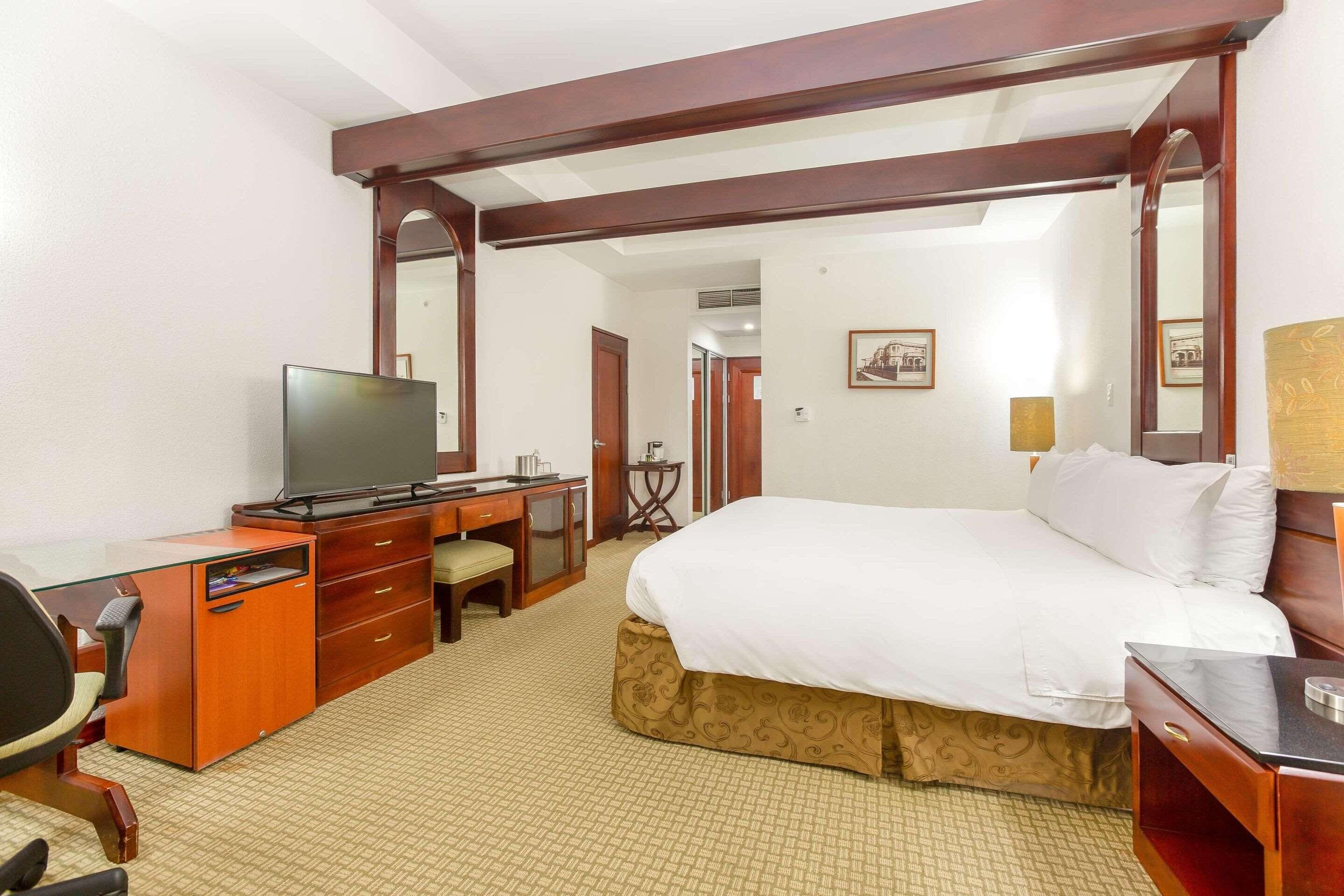 A hotel room with a bed, desk, chair, television, and a mirror.