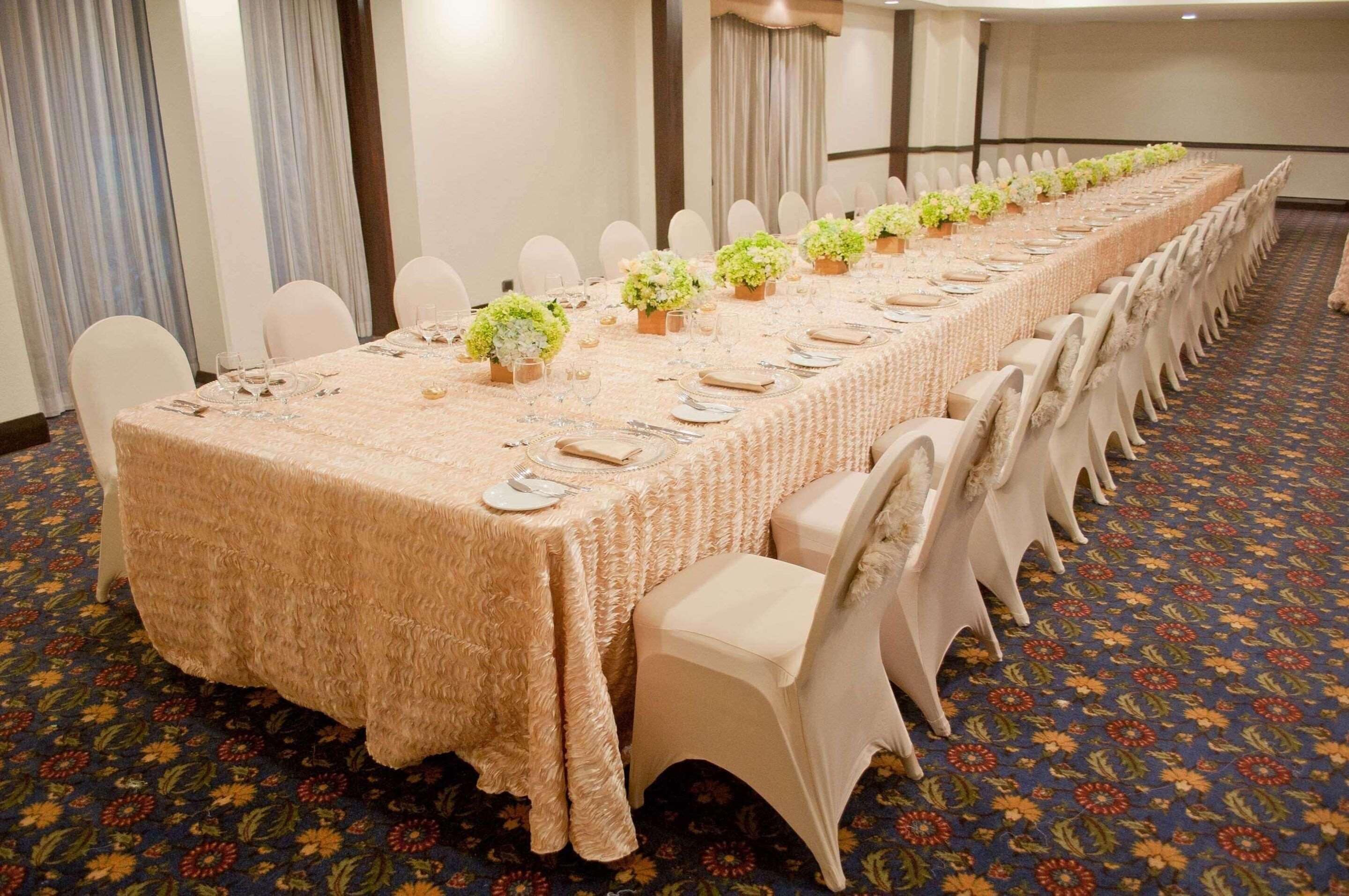A long banquet table with floral centerpieces, white chairs, and a patterned carpet.