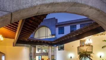 L’entrée d’un hôtel se distingue par une imposante structure en pierre en forme d’arc, un espace extérieur abrité avec des sièges, et un intérieur bien éclairé.