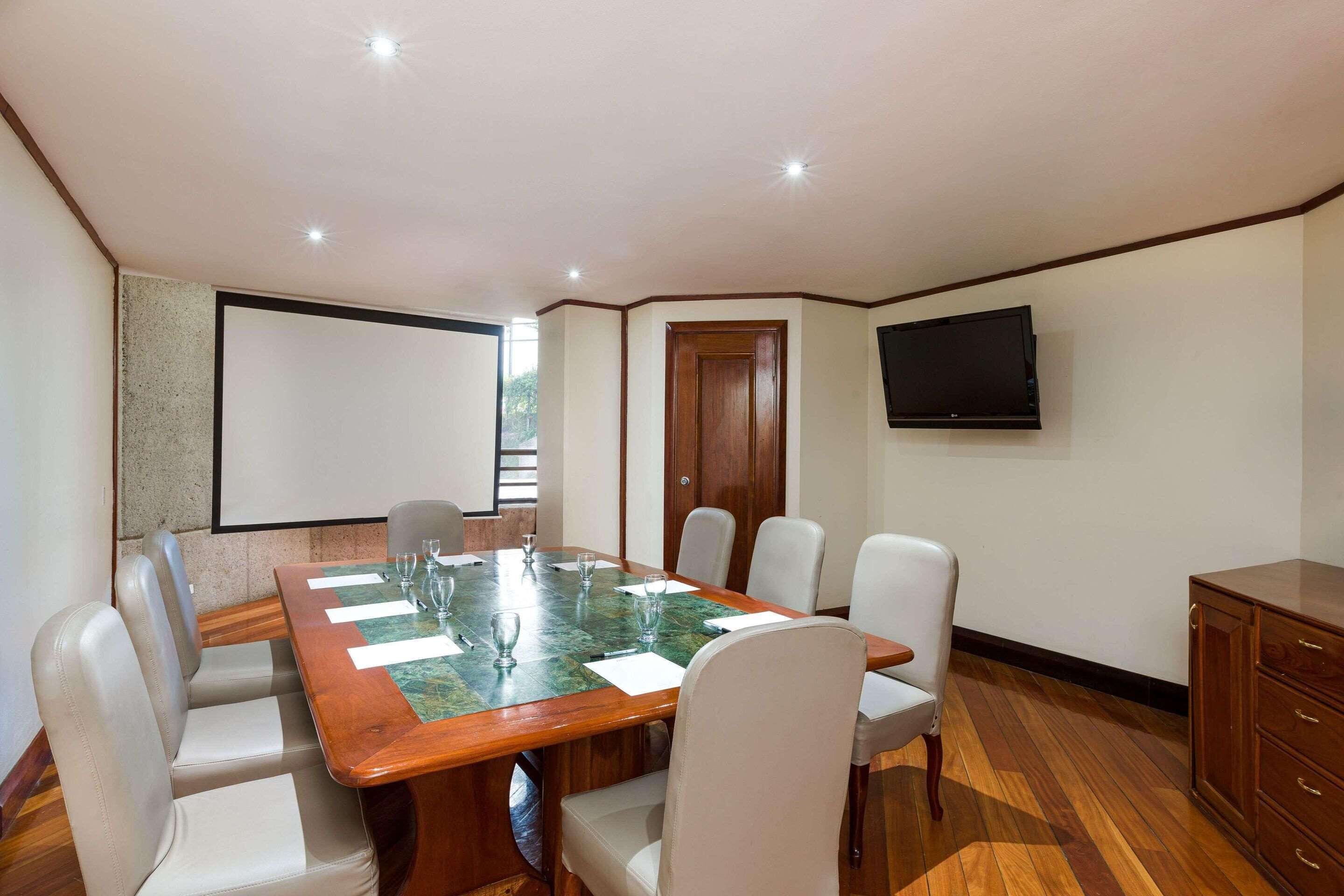 A conference room with a large table, six chairs, a television on the wall, and a wooden cabinet.