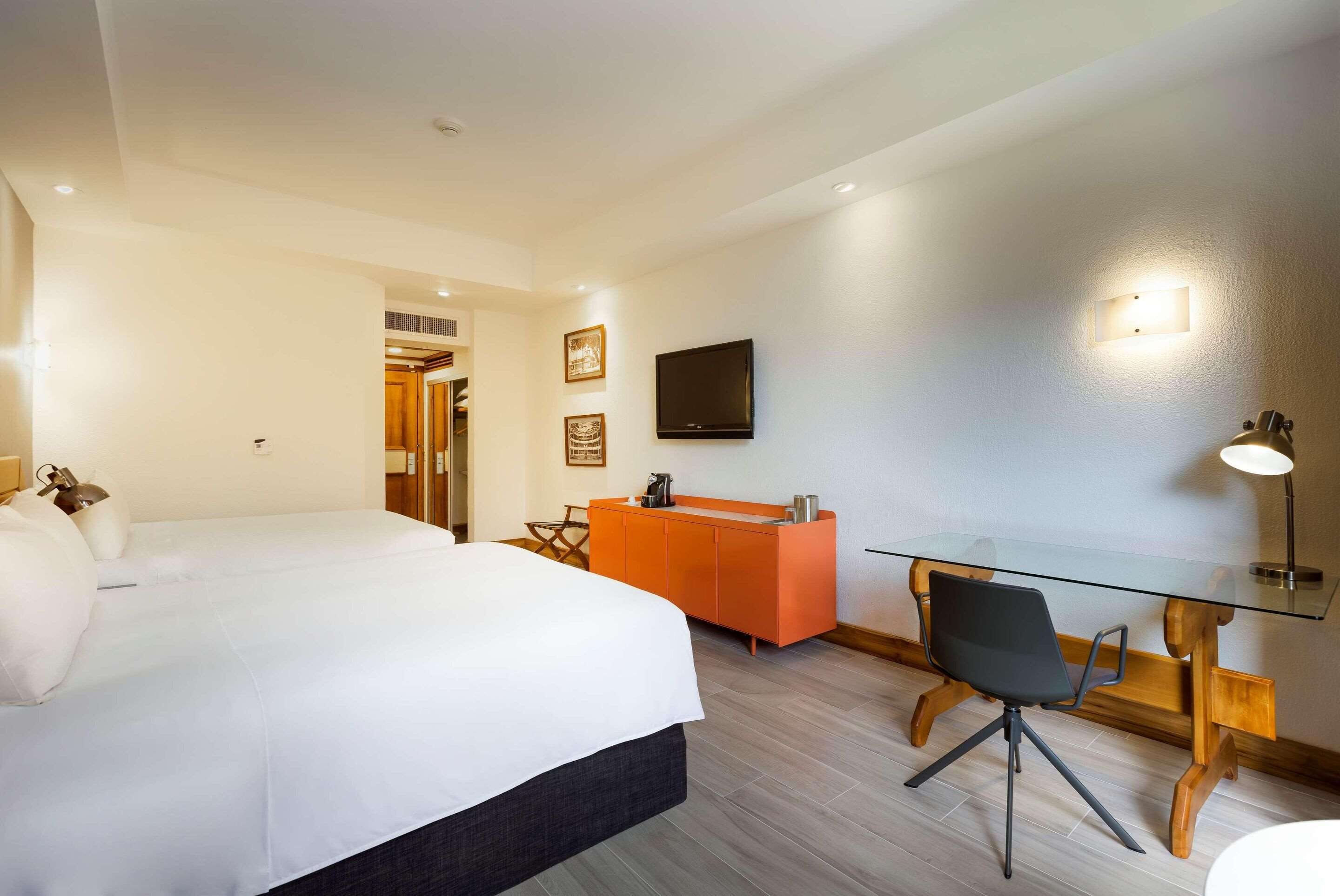 Een hotelkamer met een bed, een bureau, een stoel, een televisie en een lamp.