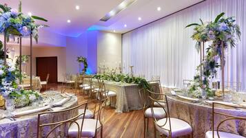 A banquet hall with round tables set for a formal event, featuring floral centerpieces and gold chairs.