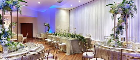 A banquet hall with round tables set for a formal event, featuring floral centerpieces and gold chairs.