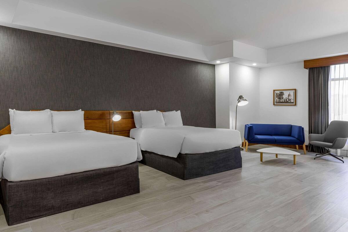 A hotel room with two beds, a blue sofa, a gray armchair, and a small table.