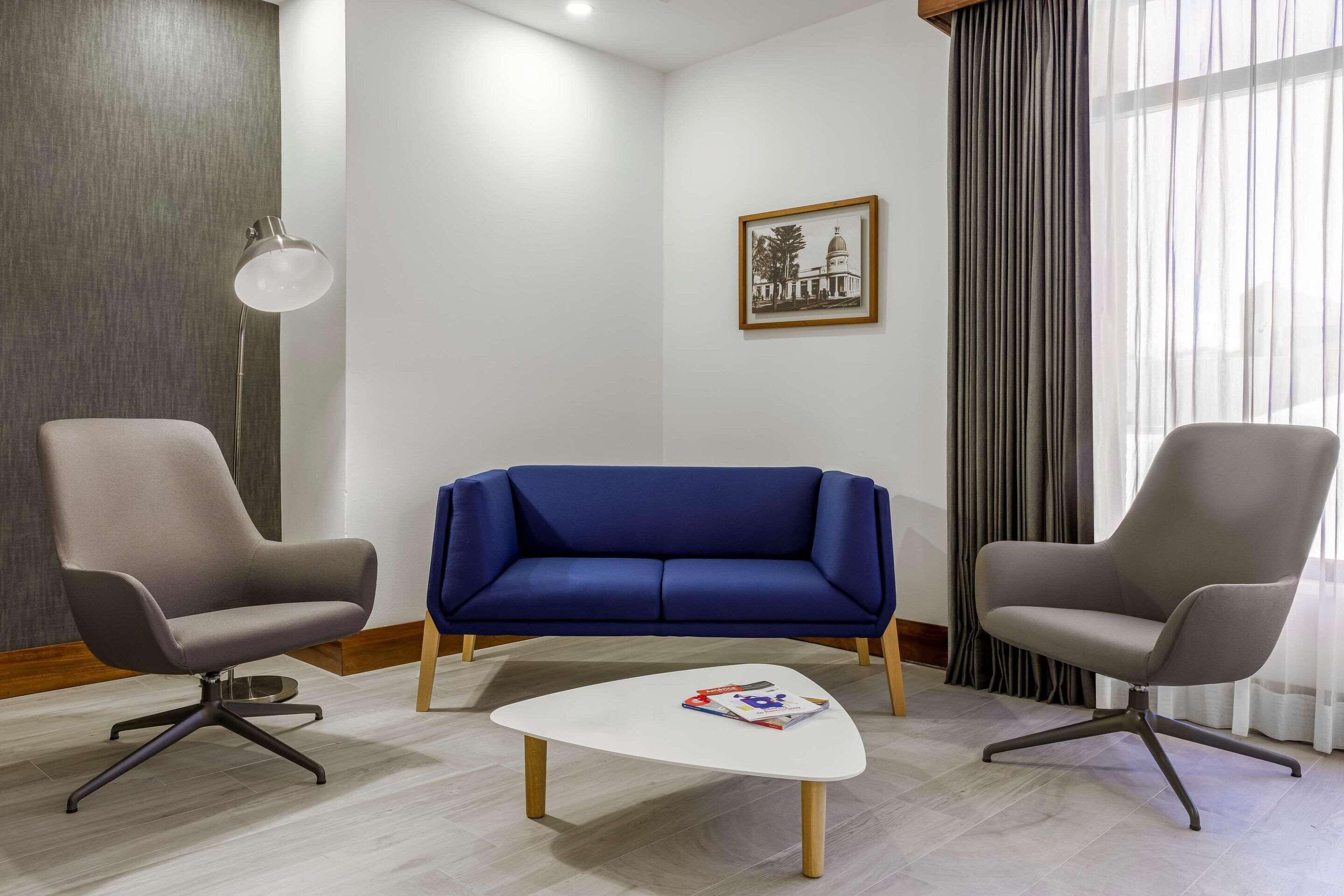 A modern room with a blue sofa, two grey armchairs, a white coffee table, a floor lamp, and a framed picture on the wall.