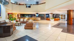 A spacious lobby with a high ceiling, multiple seating areas, a reception desk, and a staircase leading to an upper level.