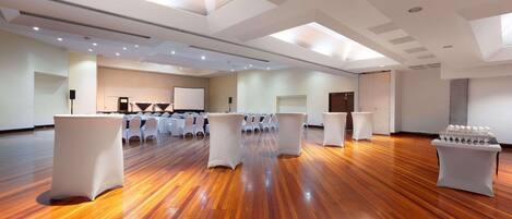 A spacious room with wooden flooring, white tables, and chairs arranged for a meeting or event.