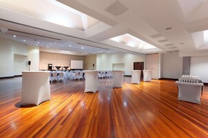 Um quarto espaçoso com piso de madeira, mesas e cadeiras brancas dispostas para uma reunião ou evento.