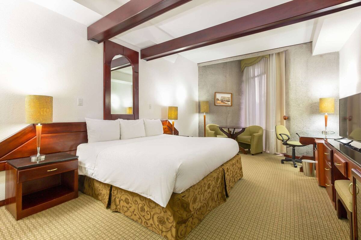 A hotel room with a large bed, a desk, a chair, and a small table.
