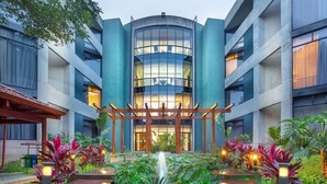 A modern building with a central glass atrium, surrounded by lush greenery and a small water feature.
