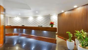 A reception area with a bench, potted plants, and a patterned wall.