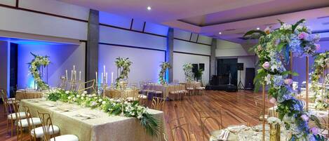 A banquet hall with round tables, chairs, and floral centerpieces.