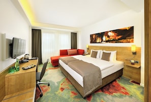 A hotel room with a bed, a desk, a television, and a large window with curtains.