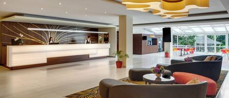 Una hall d'albergo moderna con reception, zona salotto e ampie finestre che offrono vista sull'esterno.