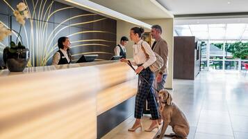 A reception area with a modern design, including a reception desk, a large vase with flowers, and a glass partition.