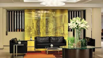 Una sala de estar moderna con un sofá de cuero negro, una mesa de centro de vidrio y un jarrón decorativo con flores blancas.