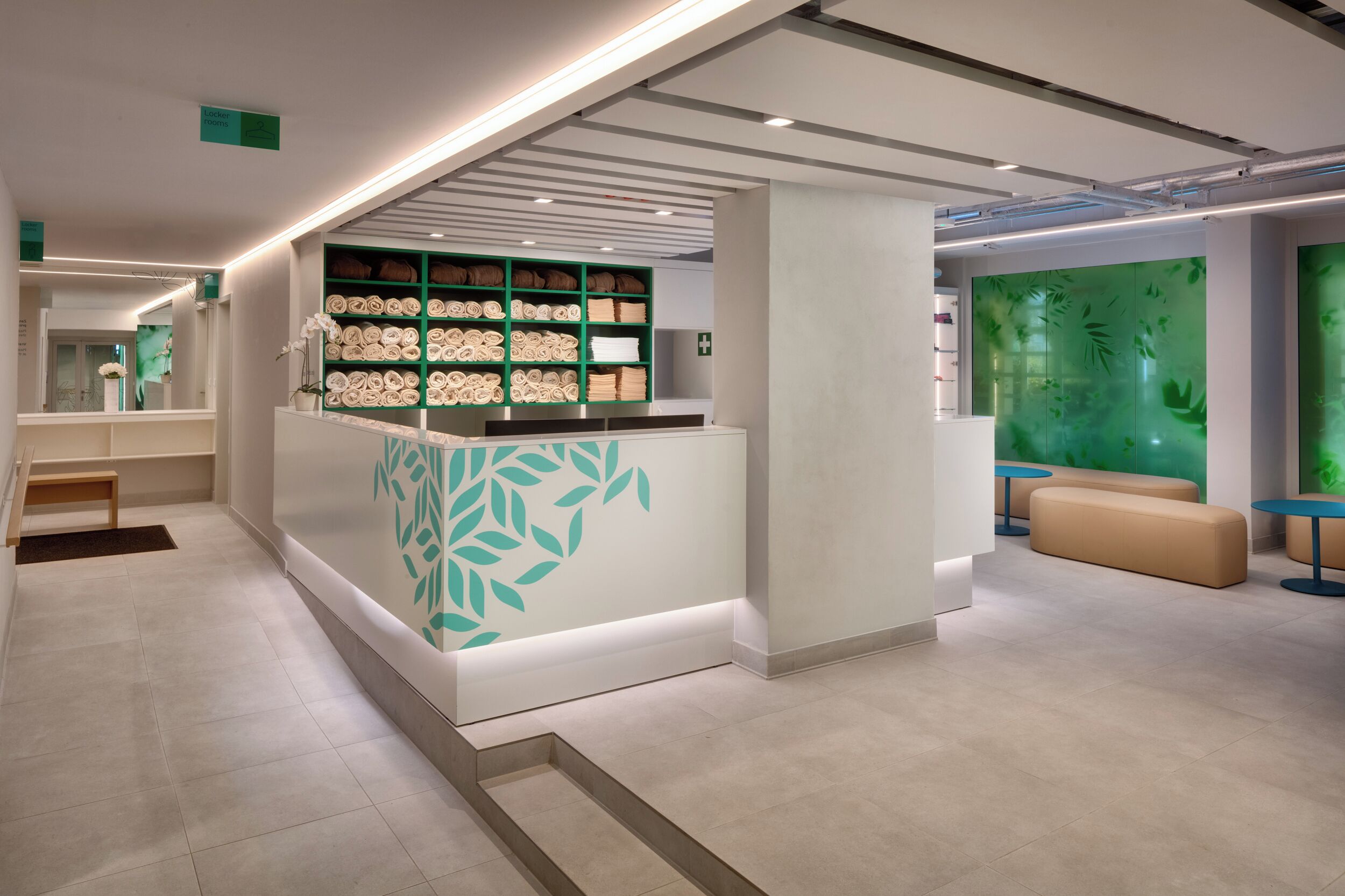 A modern hotel lobby with a reception desk, seating area, and a green wall with leaf patterns.