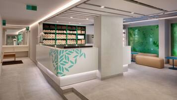 A modern hotel lobby with a reception desk, seating area, and a green wall with leaf patterns.