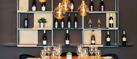 A dining area with a round table set for six, surrounded by blue chairs, with a wine rack and bottles in the background.
