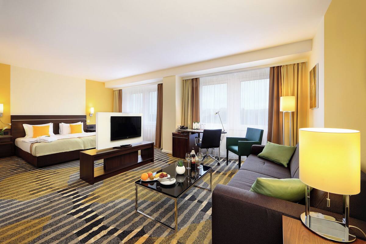 A hotel room with a bed, a TV, a sofa, a coffee table, and a desk with a chair.