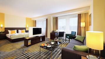 A hotel room with a bed, a TV, a sofa, a coffee table, and a desk with a chair.