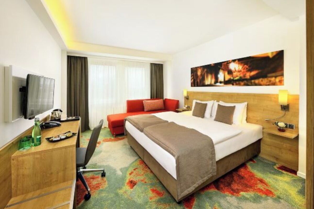 A hotel room with a bed, a desk, a TV, a sofa, and a painting on the wall.