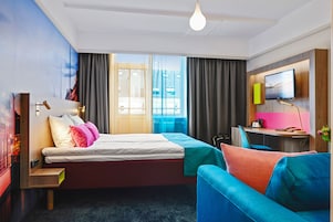 A modern hotel room with a bed, a desk, and a TV.