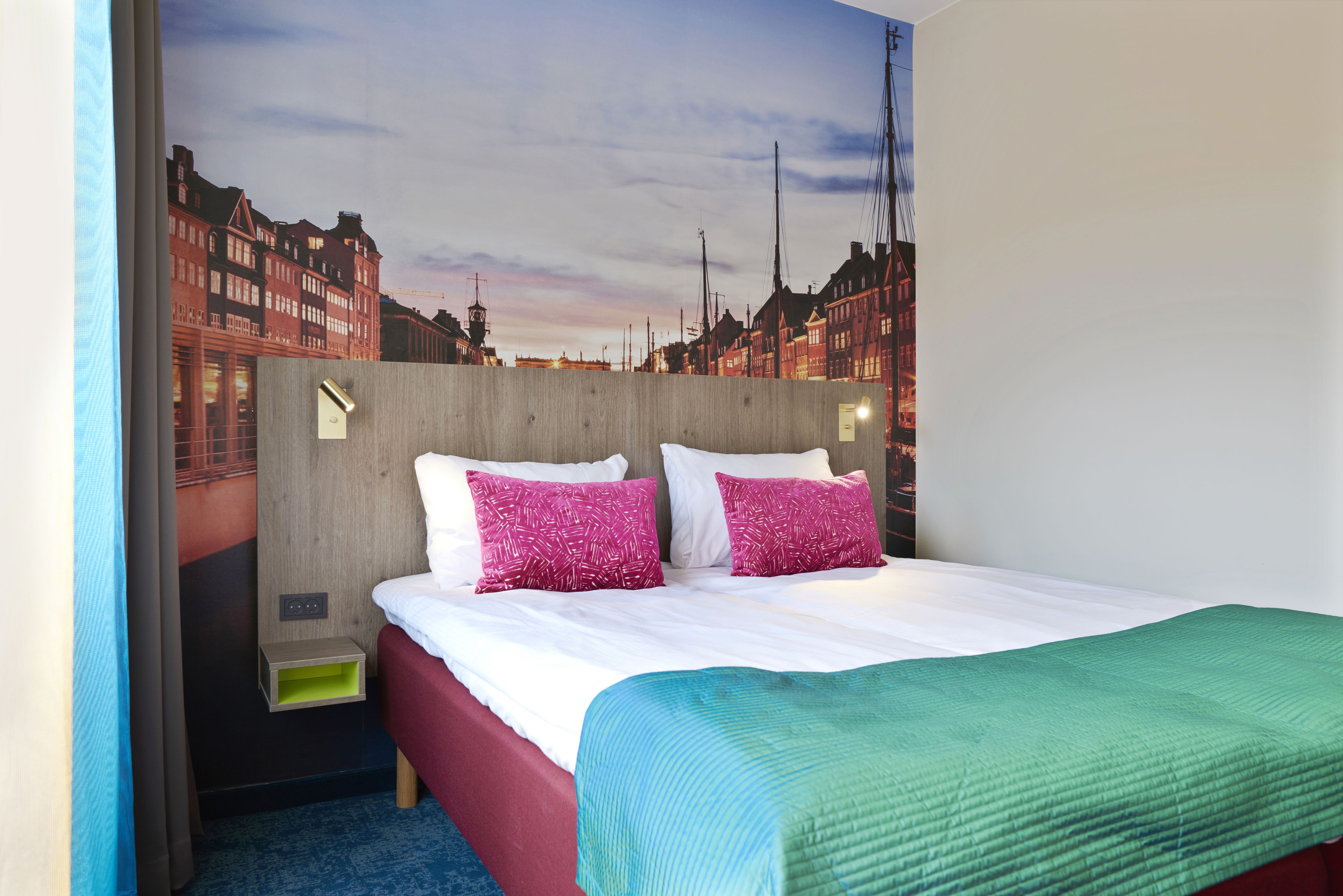 Une chambre d’hôtel avec un lit, deux oreillers, une table de chevet et une fresque murale.