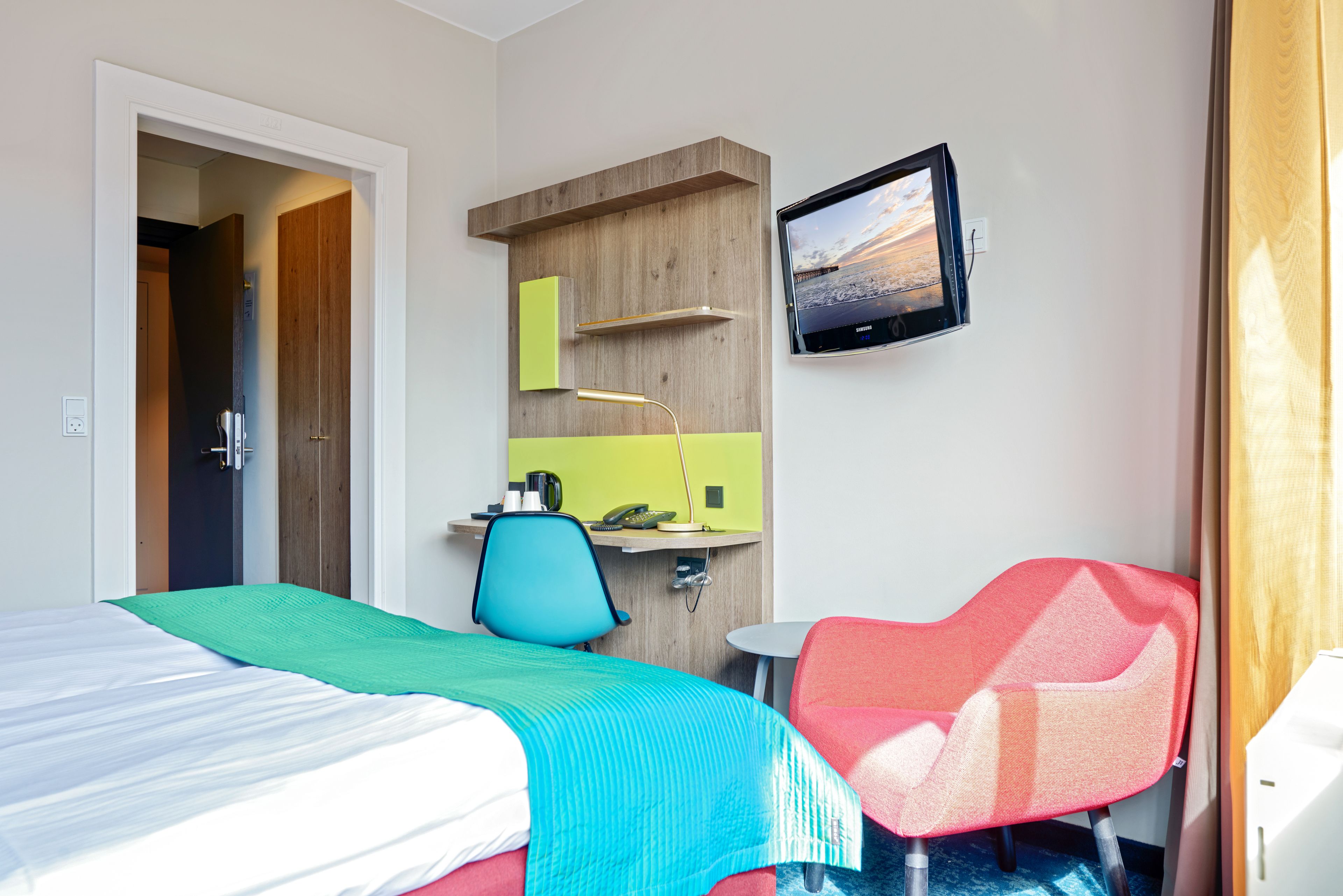 A hotel room with a bed, a desk with a chair, a television, and a small table.